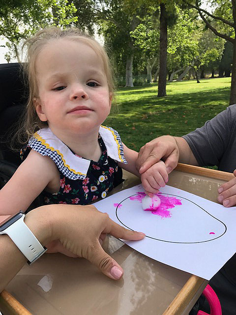 A little girl is painting with pink color using a cotton ball