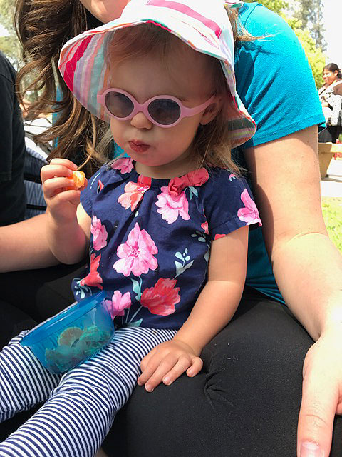 A child is sitting on her mother's lap eating orange slices at Park Day