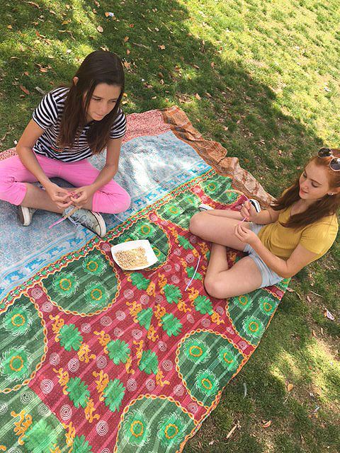 Two girls are sitting together and eating lunch on a blanket in the grass at Park Day