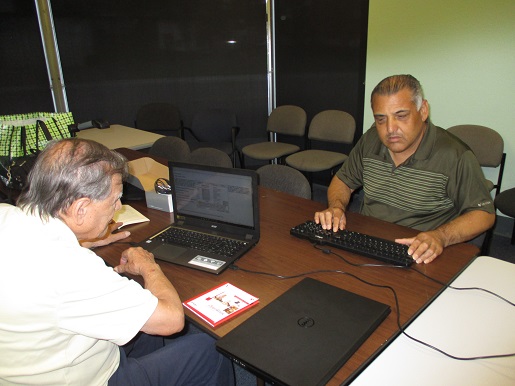 Ciro Trujillo is teaching Rafael Lopez how to use his laptop.